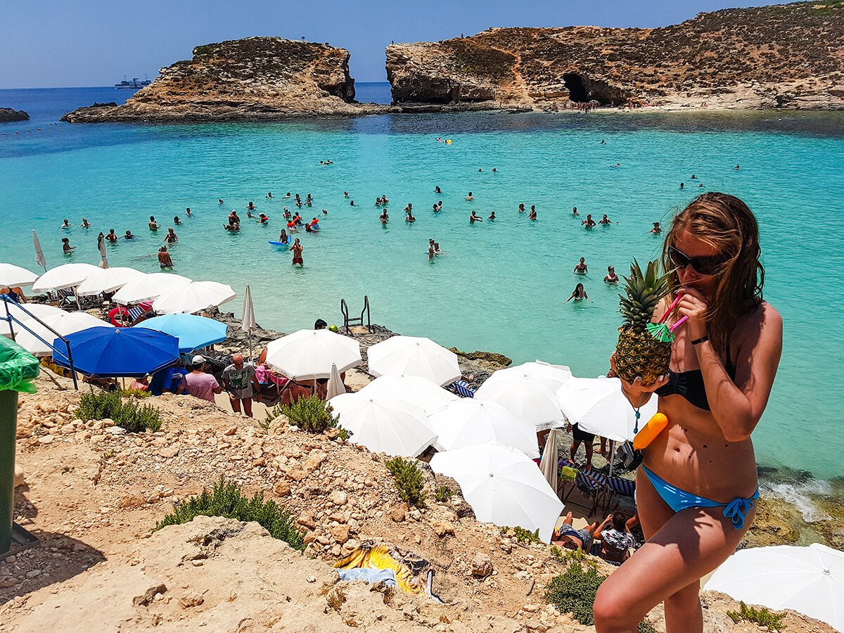 Woman in swimsuit sipping ananas with the blue lagoon in the background at Comino, Malta