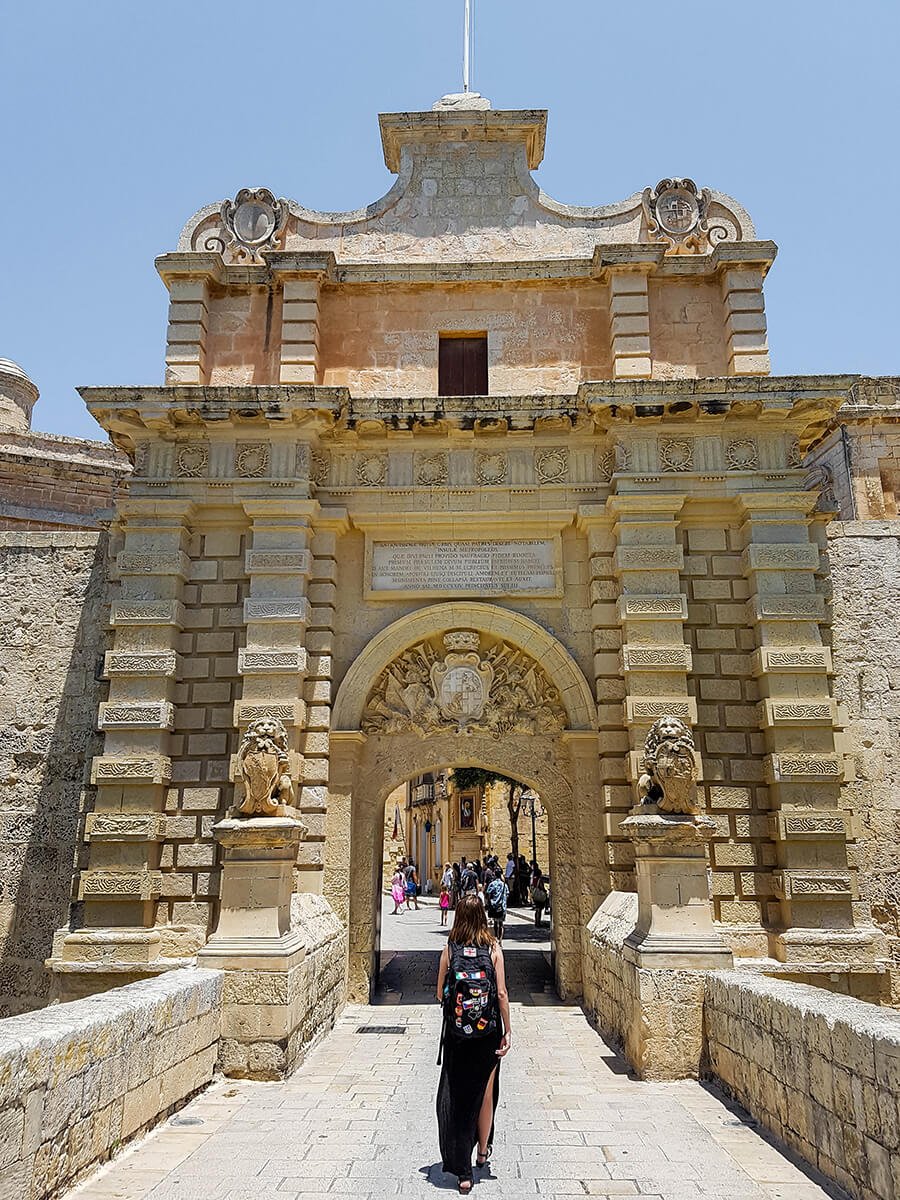 A backpacker in dress in front of the entrance to Mdina