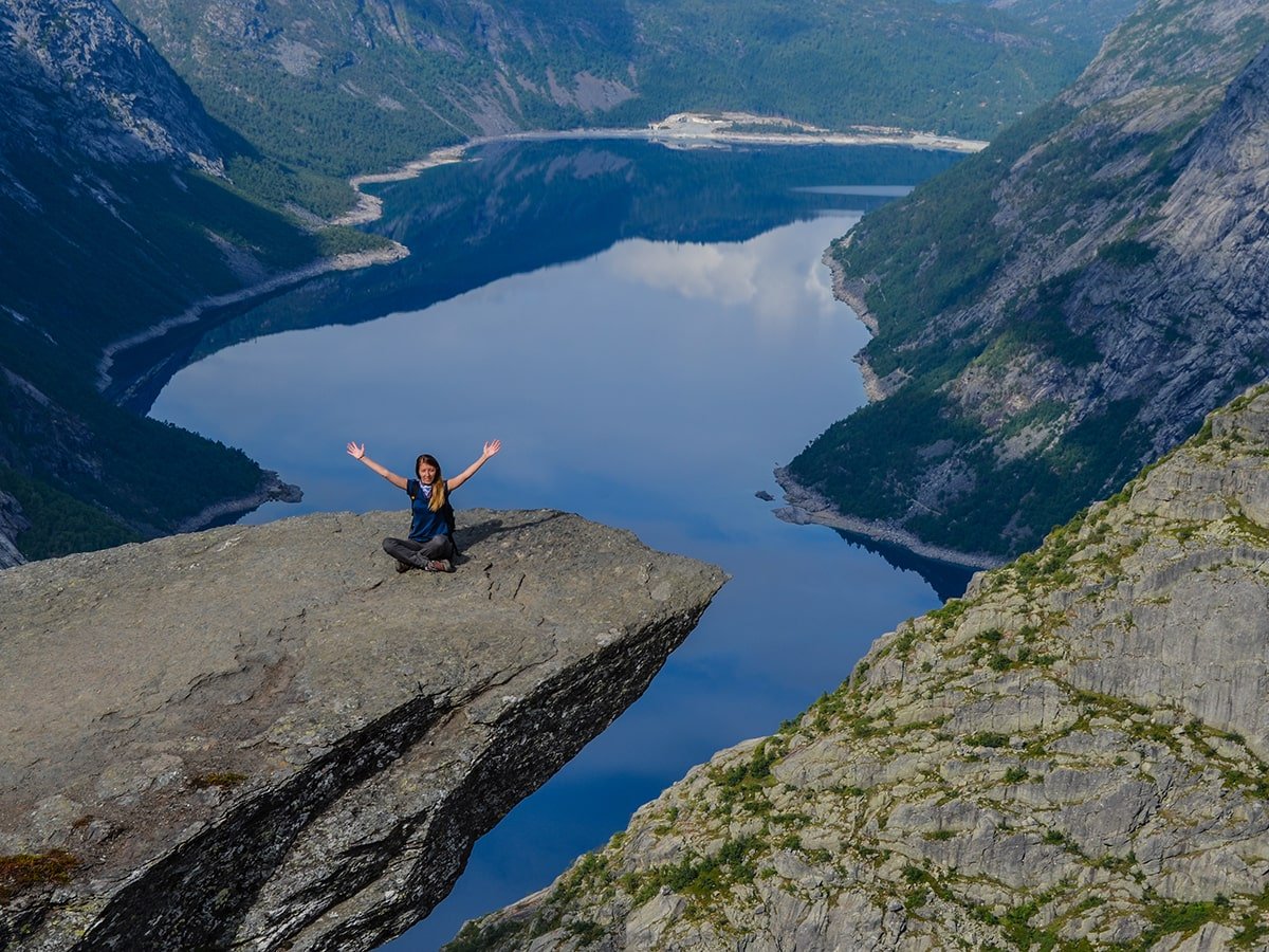 Sitting on the "Troll's tongue" while below the beautiful fjord reflects the high mountains surrounding it (Hiking Trolltunga)