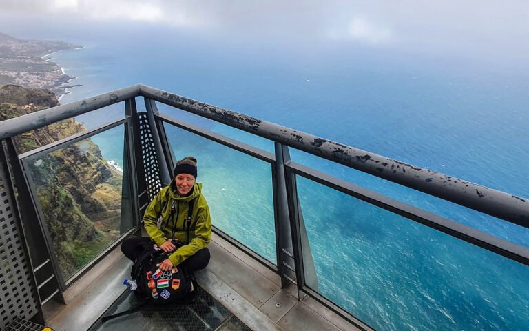 Me sitting on the glass floor in green jacket at the Cabo Girao viewpoint