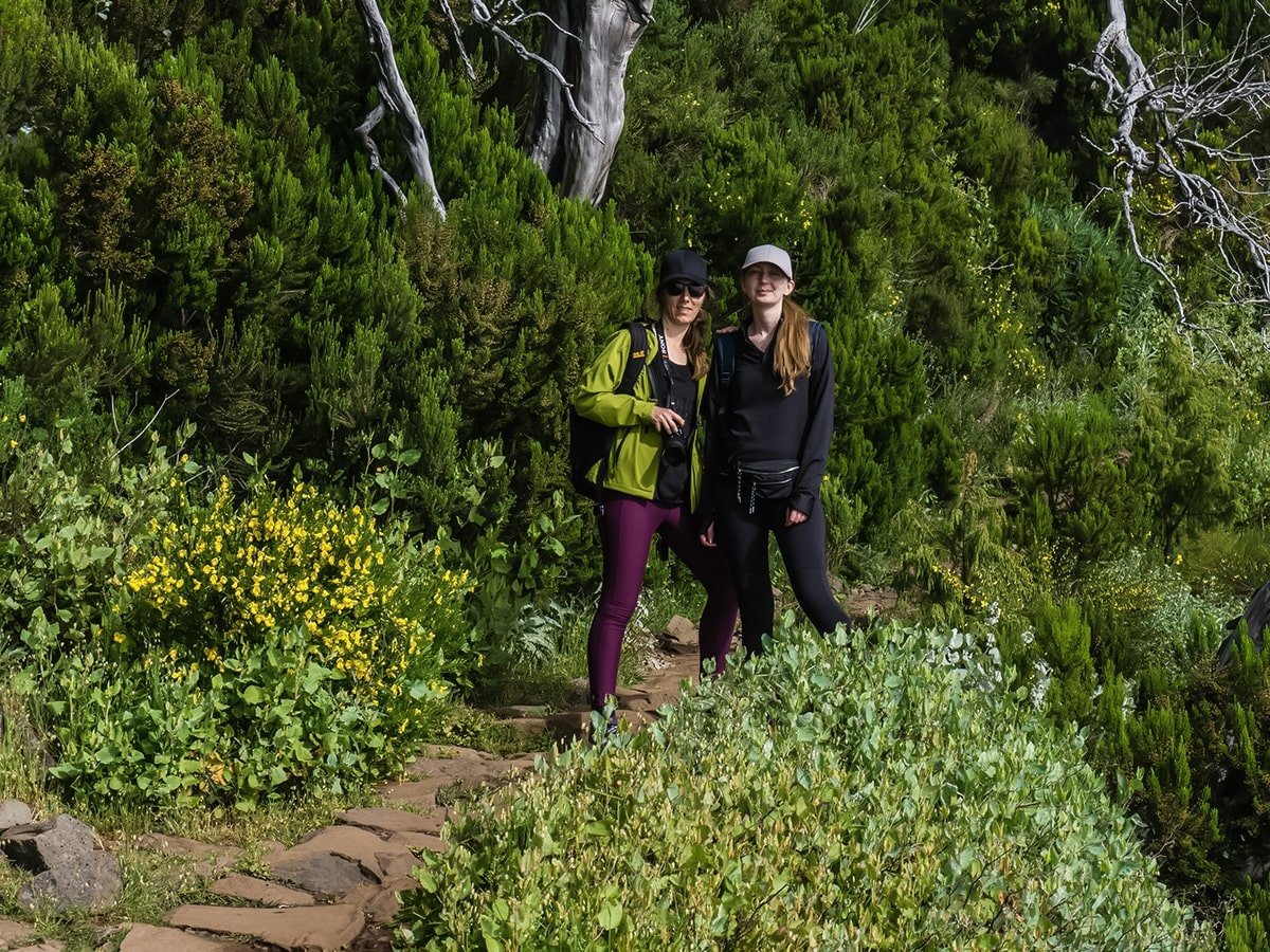 Two girls on the trail, stopping to take a photo with the lush vegetation