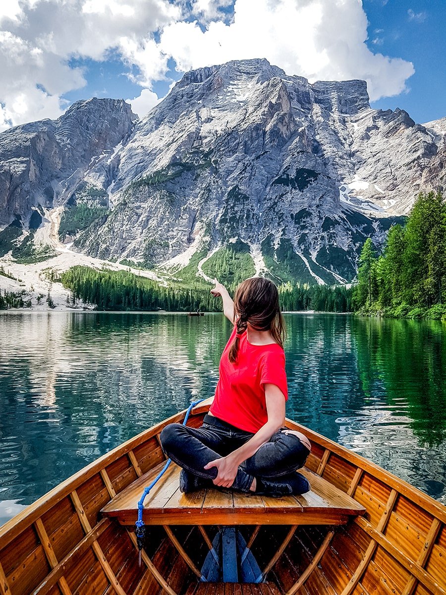 A girl in red t-shirt in a boat at lake Braies pointing towards the mountains