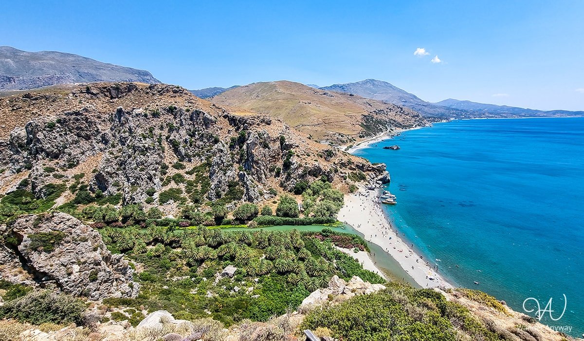 Palm trees lining the sandy shores of Preveli Palm Beach, with turquoise waters and rocky cliffs in the background.