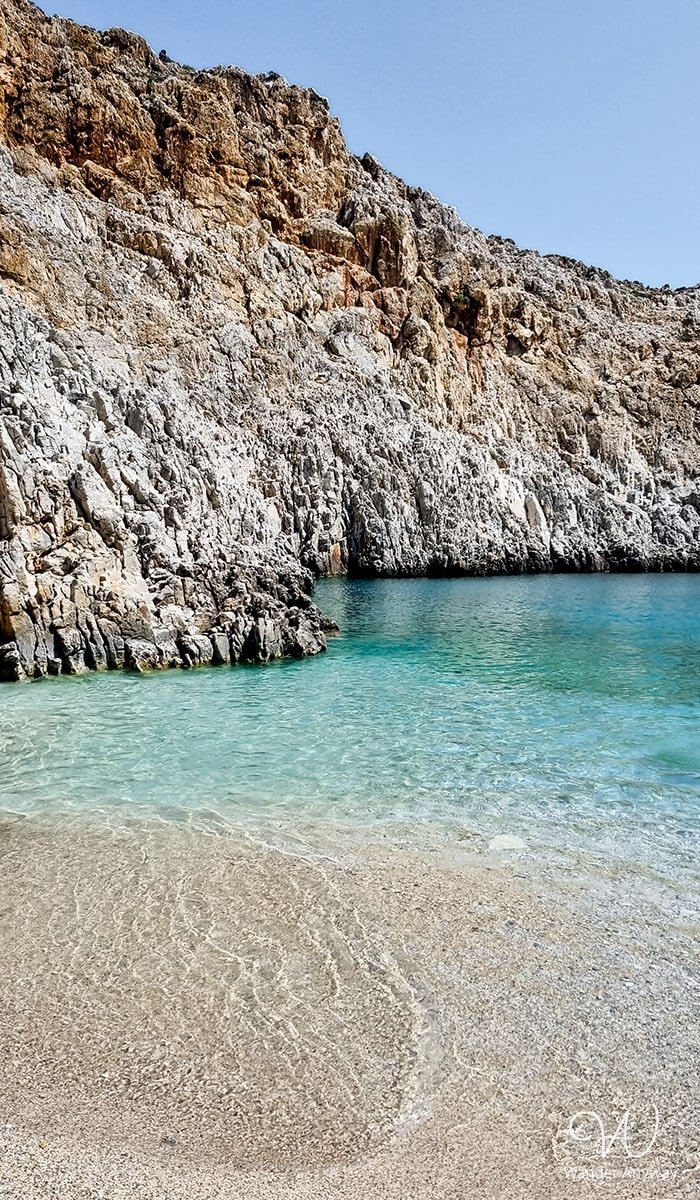 A scenic view from the shore of Seitan Limania Beach, highlighting the stunning contrast between the crystal-clear turquoise waters and the dramatic limestone cliffs that frame the bay