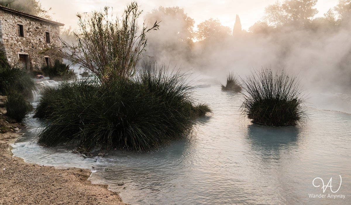 Early morning view of Cascate del Mulino hot springs with mist rising from the natural limestone pools