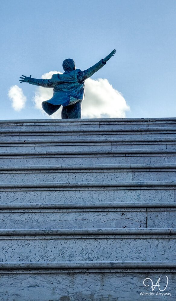 Bronze statue of Domenico Modugno with arms raised beside the sea in Polignano a Mare.