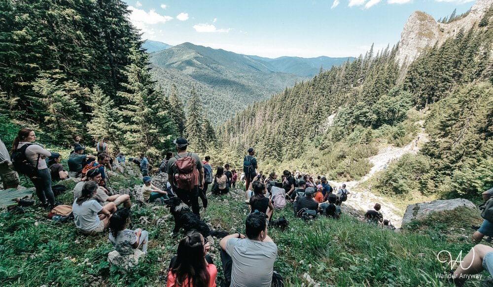 Hikers taking a break on a grassy slope in Piatra Craiului National Park, overlooking the Carpathian Mountains during a group hike event.